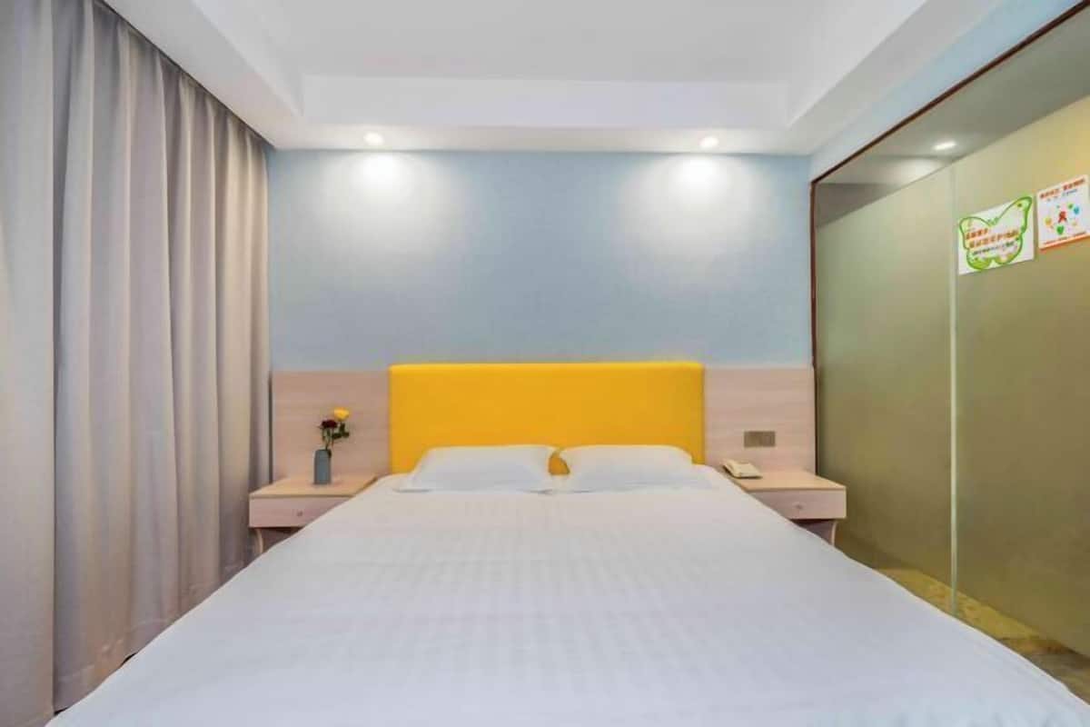 A hotel room with a bed, two bedside tables, a nightstand, a wall with a mirror, and a curtain.