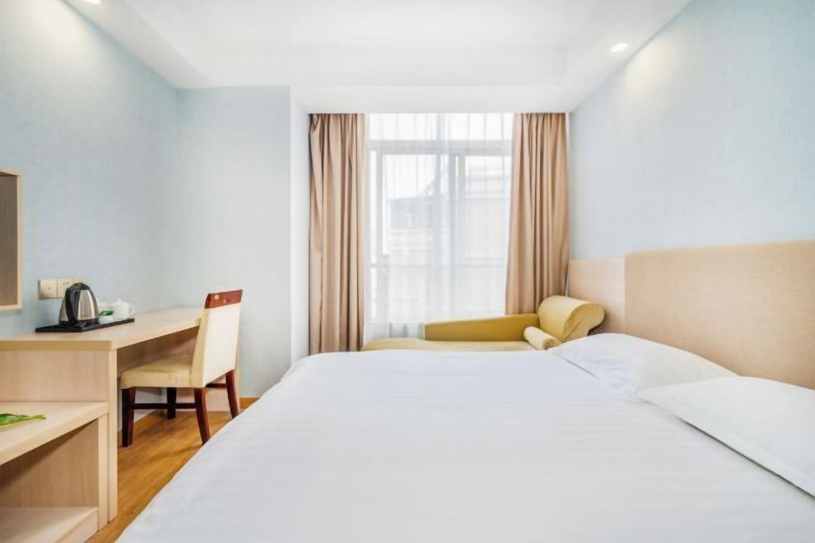 Une chambre d’hôtel avec un lit, un bureau, une chaise et une fenêtre avec des rideaux.