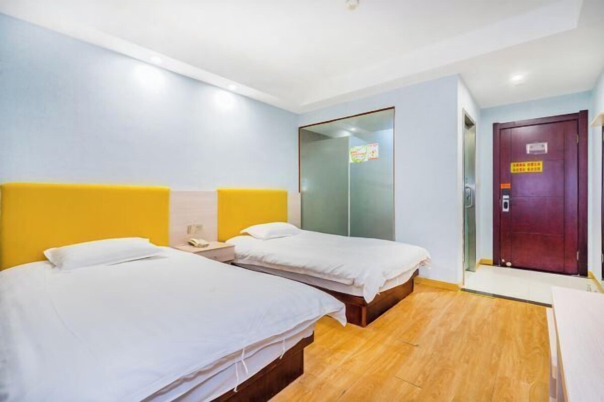 A hotel room with two beds, a wooden floor, a glass door, and a wooden door with a sign.