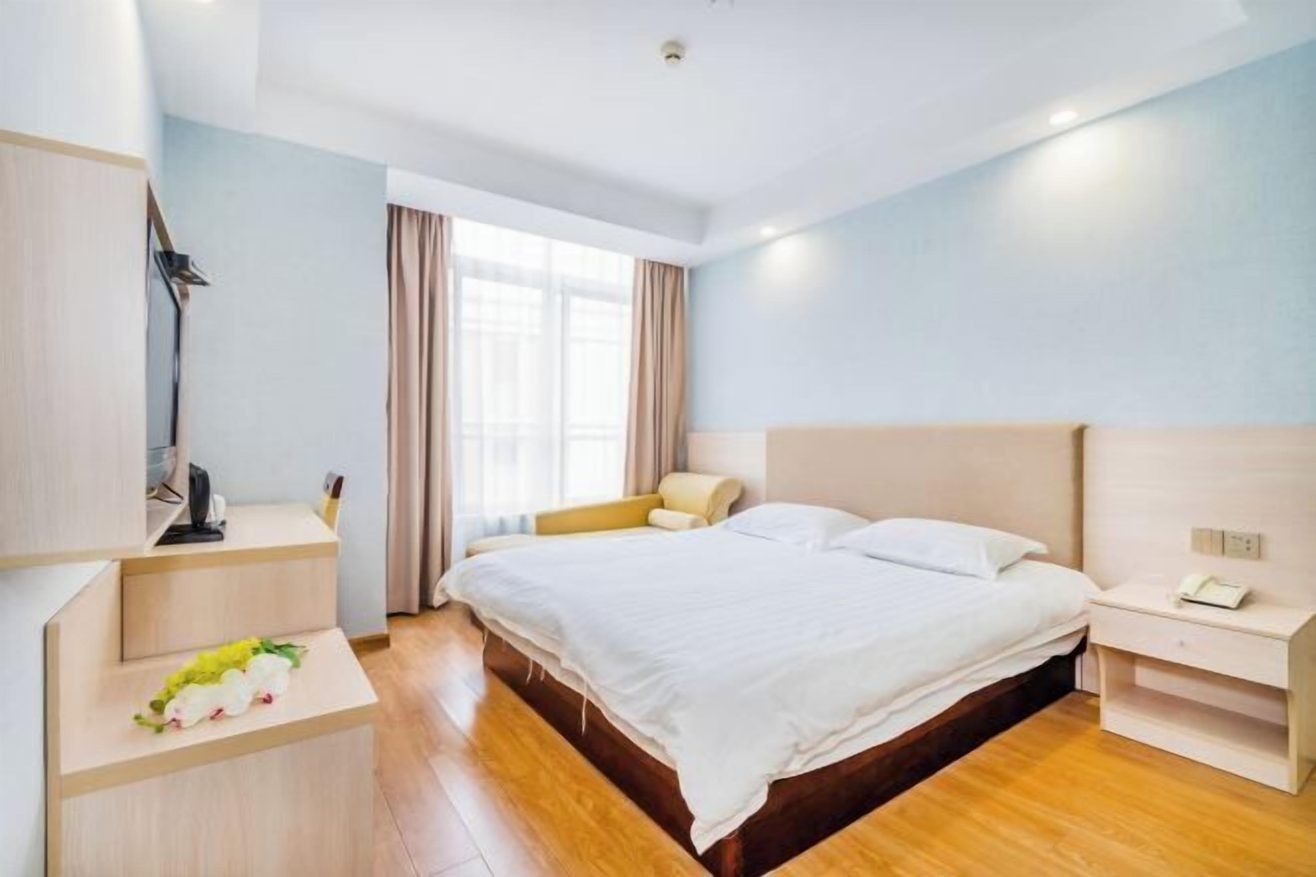 Une chambre d’hôtel avec un lit, une table de chevet, une lampe et une fenêtre avec des rideaux.