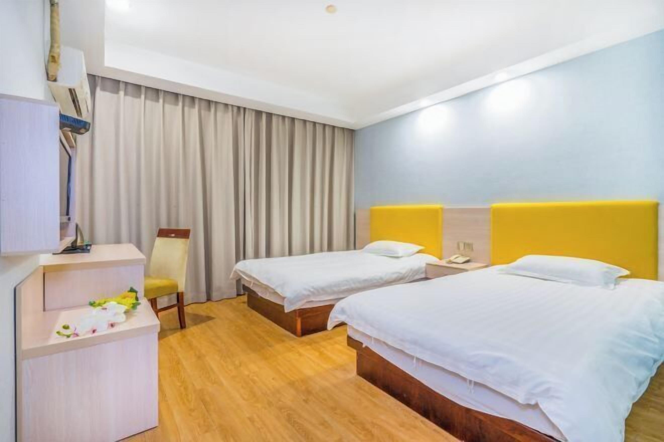 A hotel room with two single beds, a desk, a chair, and a large window with curtains.
