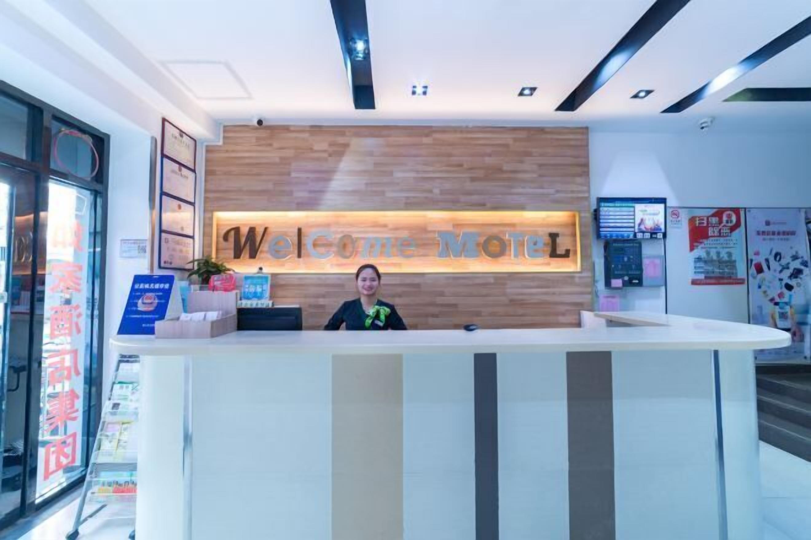 A reception desk with a "Welcome Motel" sign, a digital display, and a customer service counter.