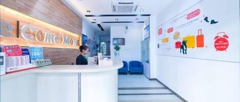 A hotel reception area with a wooden reception desk, a digital screen, and a wall with travel-related graphics.