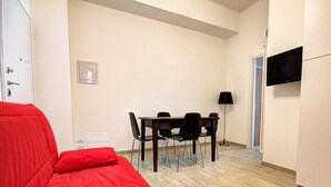 A room with a bed, a dining table with chairs, a TV mounted on the wall, and a door leading to another room. - Appartamento Ariel   La Perla del Mare di Polignano (Polignano a Mare)
