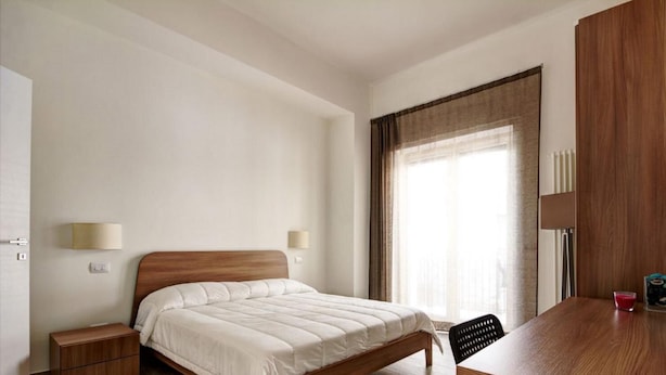 A hotel room with a wooden bed, a desk with a chair, a TV, and a window with curtains. - Appartamento Ariel   La Perla del Mare di Polignano (Polignano a Mare)