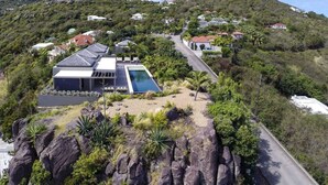 Una casa moderna con piscina, rodeada de vegetación exuberante y colinas.