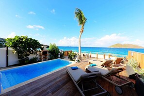 Un espace aménagé au bord de la piscine, avec une terrasse en bois, des chaises longues et une vue sur l’océan.