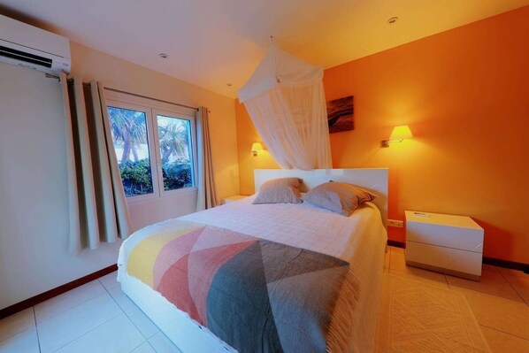 Une chambre à coucher comprenant un lit, une table de chevet, une fenêtre avec des rideaux et une lampe fixée au mur.
