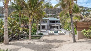 Ein modernes, zweistöckiges Haus mit Pool, umgeben von Palmen und einem Sandstrand.