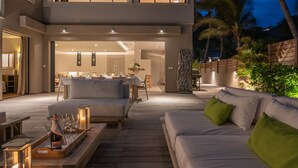 A modern outdoor dining area with a wooden deck, a sofa, and a table set for a meal. - Beautiful Villa K Luxury villa (Anse Des Cayes)