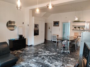 Cozinha moderna com armários brancos, área de jantar com mesa de vidro e um sofá de couro preto.