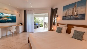A hotel room with a large bed, a desk, and a balcony with outdoor seating. - Au Coeur du Rocher (1/3 Rooms) (Marigot)