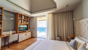 Une chambre avec un grand lit, une bibliothèque en bois, une télévision et une vue sur la mer.