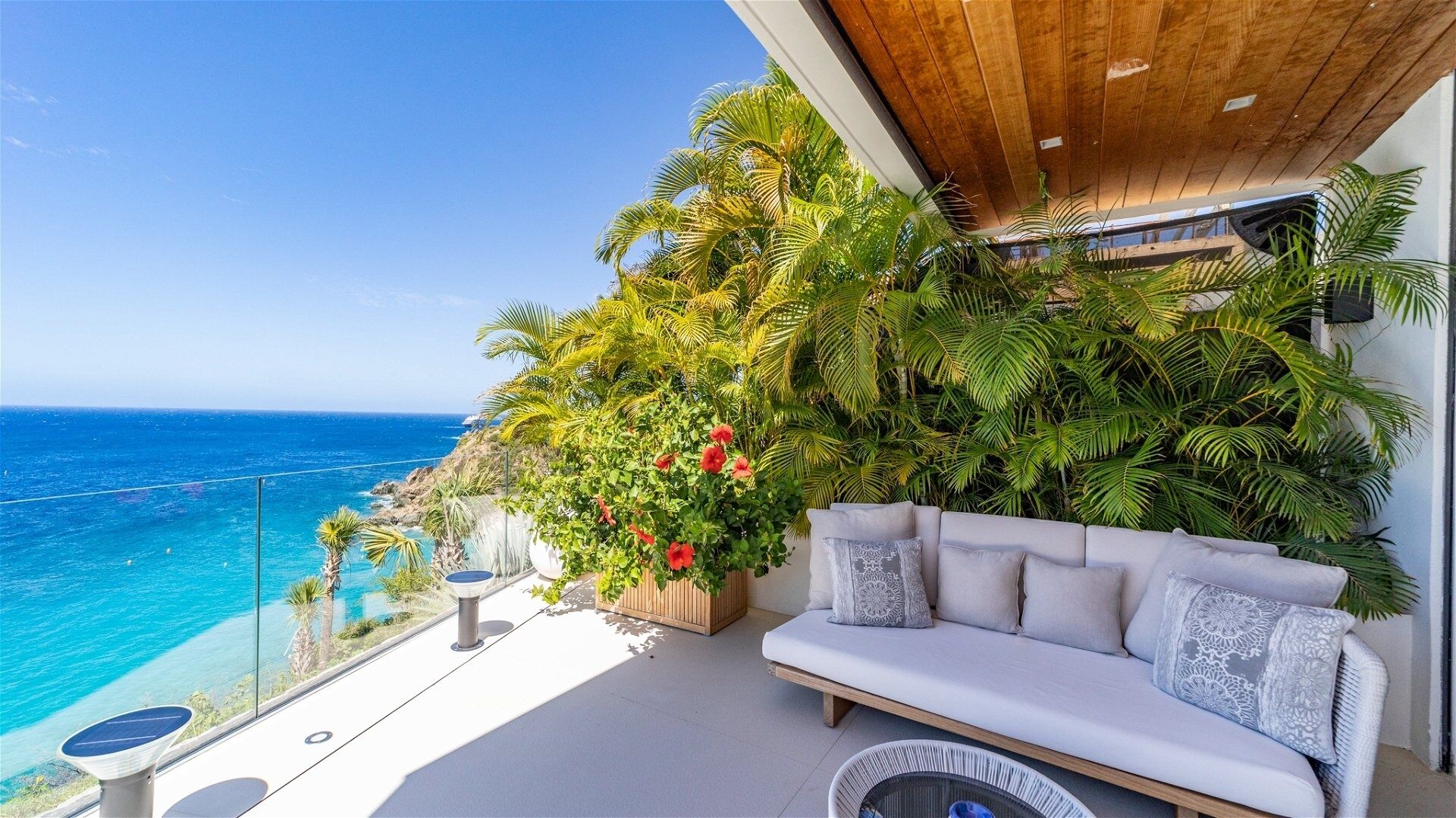 Un balcone con vista sull'oceano, un divano bianco e vegetazione rigogliosa.