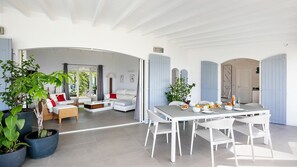 Un vaste espace de vie comprenant un canapé blanc, une table à manger dressée avec des assiettes et des verres, et des plantes en pot.