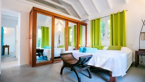 Une chambre d’hôtel avec un lit, un bureau et une chaise. On y trouve un grand miroir et une fenêtre avec des rideaux.