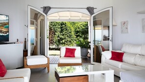 Una sala de estar moderna con muebles blancos, una mesa de centro de vidrio y vistas a un jardín exuberante a través de puertas abiertas.