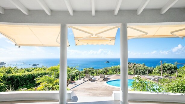 Vista de la piscina con una clara vista al océano, una terraza de madera y un área de estar cubierta.