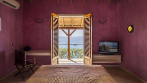 Quarto com cama, televisão e vista para o mar por entre as grades abertas.