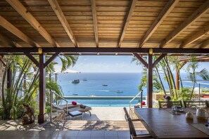 Un espace extérieur abrité comprenant une piscine, des chaises longues et une vue sur l’océan, où l’on peut apercevoir des bateaux.