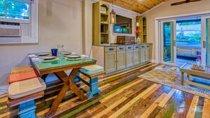 Une pièce avec un plancher en bois, une table à manger avec des chaises, un buffet et une vue sur l’extérieur à travers des portes vitrées.