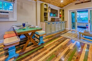 Quarto com piso de madeira, uma mesa de jantar com cadeiras, um armário e vista através de portas de vidro.