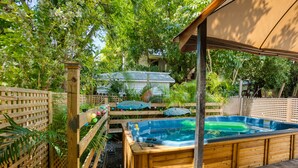 Un bain à remous en bois, entouré d’une clôture en bois et d’une végétation luxuriante.