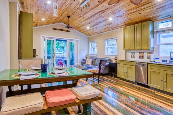 Uma cozinha ampla com piso de madeira, uma área de refeições com mesa de vidro e vista para o exterior.