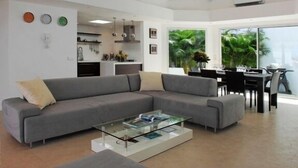 Una sala moderna con un sofá seccional gris, una mesa de centro de vidrio y un comedor con mesa y sillas negras.