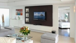 Una sala de estar moderna con un televisor de pantalla plana grande montado en una pared oscura, una mesa de centro de vidrio con un jarrón de flores y un sofá gris.