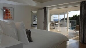Un dormitorio con una cama grande, un cuadro en la pared y vistas a un balcón con mobiliario exterior.