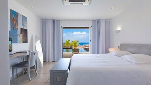Une chambre d’hôtel avec un lit, un bureau, une chaise et une vue sur l’océan et les palmiers.