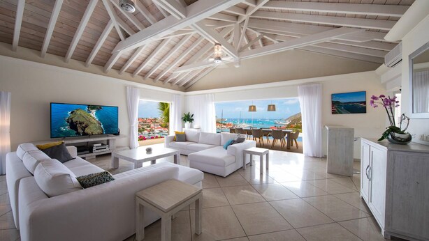 Un salon spacieux avec une grande télévision, des canapés blancs et une vue sur la mer.