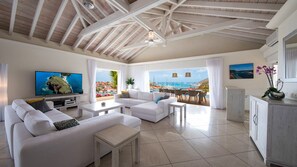 Un salon spacieux avec une grande télévision, des canapés blancs et une vue sur la mer.