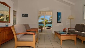 Ein Wohnzimmer mit Korbmöbeln, Meerblick durch eine Glastür und ein gerahmtes Bild an der Wand.