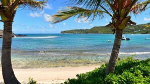 Ein Strand mit klarem türkisblauem Wasser, Palmen und Booten in der Ferne.