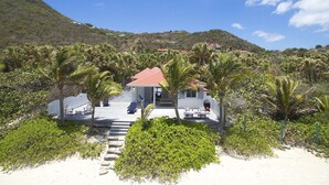 Ein Hotel direkt am Strand mit einem Haus mit rotem Dach, einer Terrasse mit Liegestühlen und einer Treppe zum Eingang.
