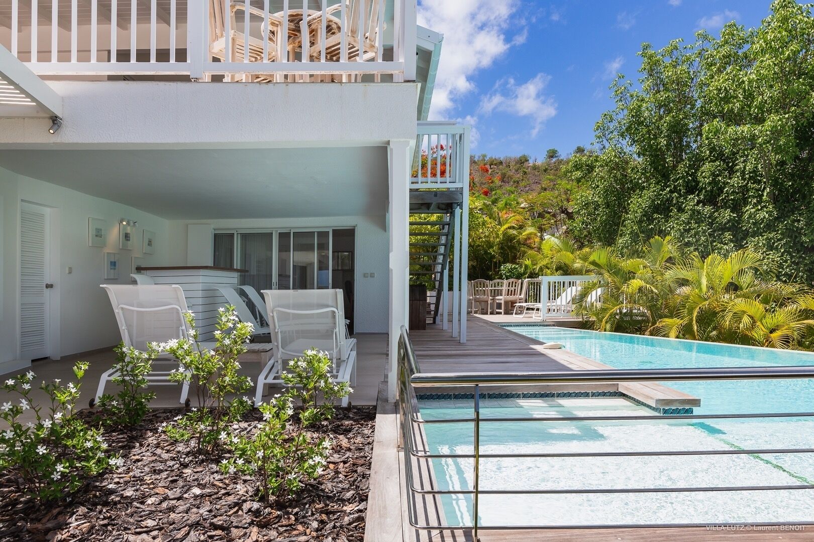Ein modernes, zweistöckiges Haus mit Pool, Sitzgelegenheiten im Freien und üppigem Grün.