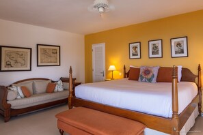 A bedroom with a large bed, a sofa, and a bench. There are framed pictures on the wall.