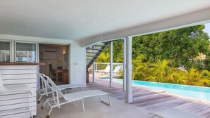 Ein überdachter Außenbereich mit Pool, Liegestühlen und einer Treppe zu einer Terrasse.