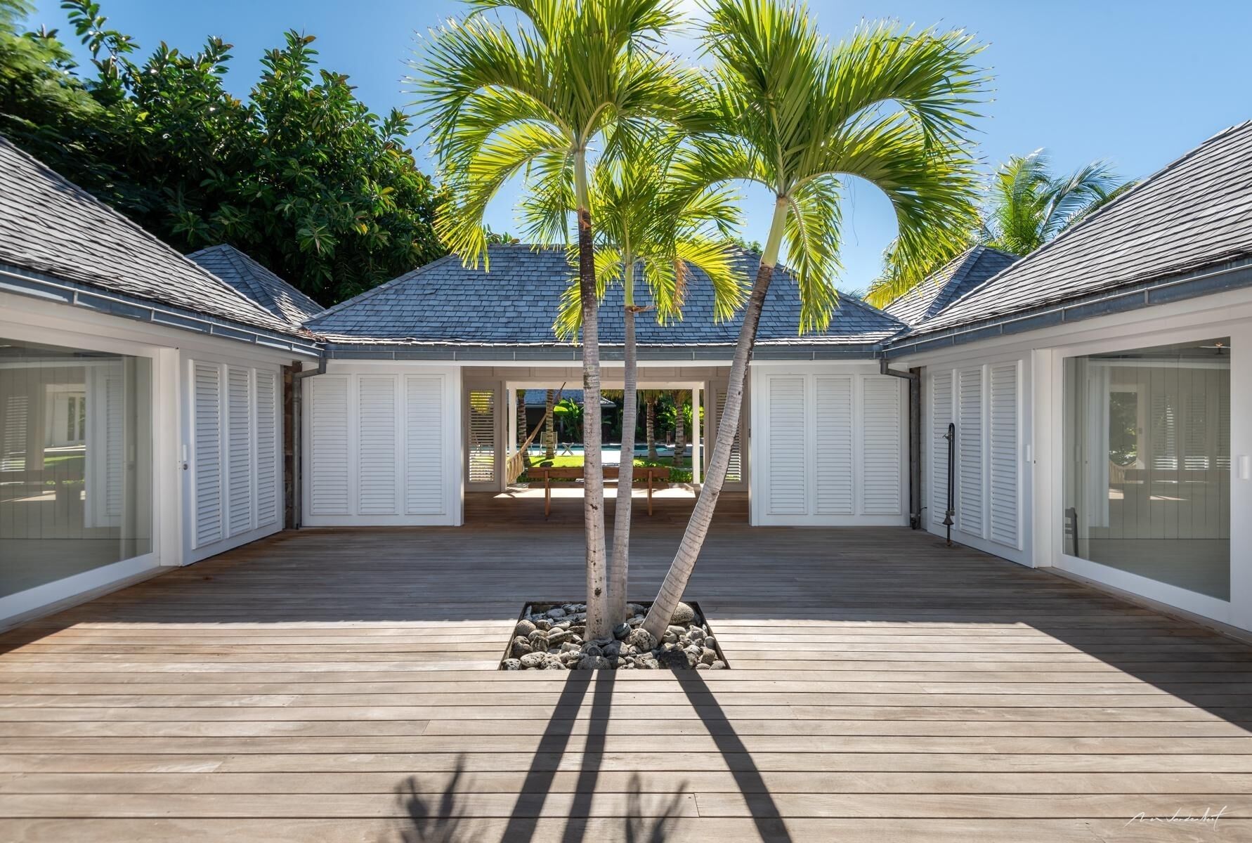 Una casa moderna con terraza de madera, dos palmeras y un área de patio techada.