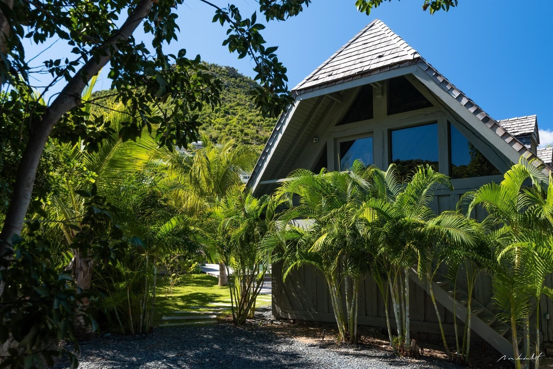 Une maison avec un toit en pente, entourée d’une végétation luxuriante et de palmiers.
