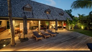 Ein modernes Haus mit überdachter Terrasse, Liegestühlen und einem gut beleuchteten Innenraum.
