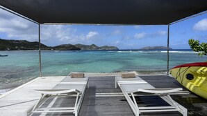 Eine überdachte Terrasse mit zwei Liegestühlen und einem Kajak, mit Blick auf türkisfarbenes Wasser und entfernte Inseln.