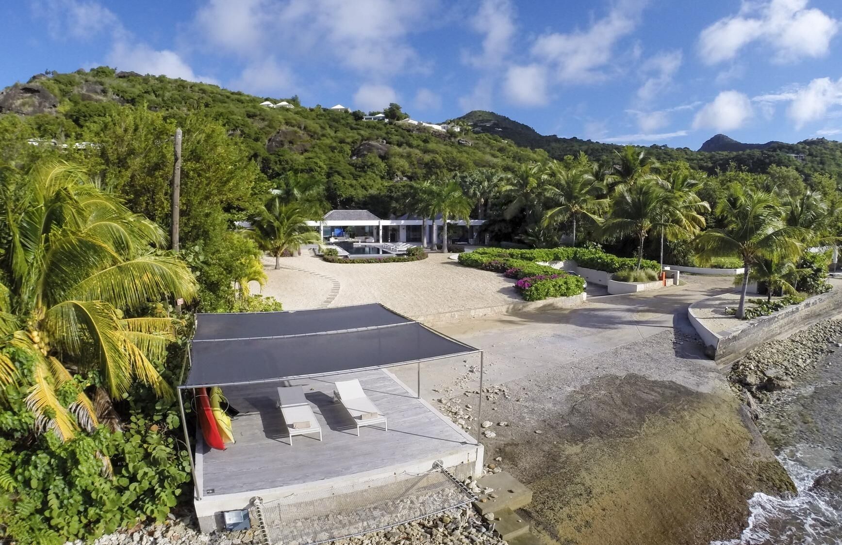 Um resort à beira-mar com área de estar coberta, piscina e vegetação exuberante.