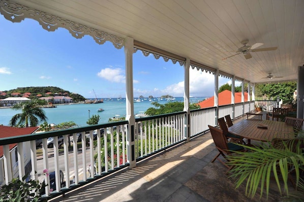Un espace extérieur abrité, avec vue sur la mer, comprenant une table avec des chaises et une rambarde.