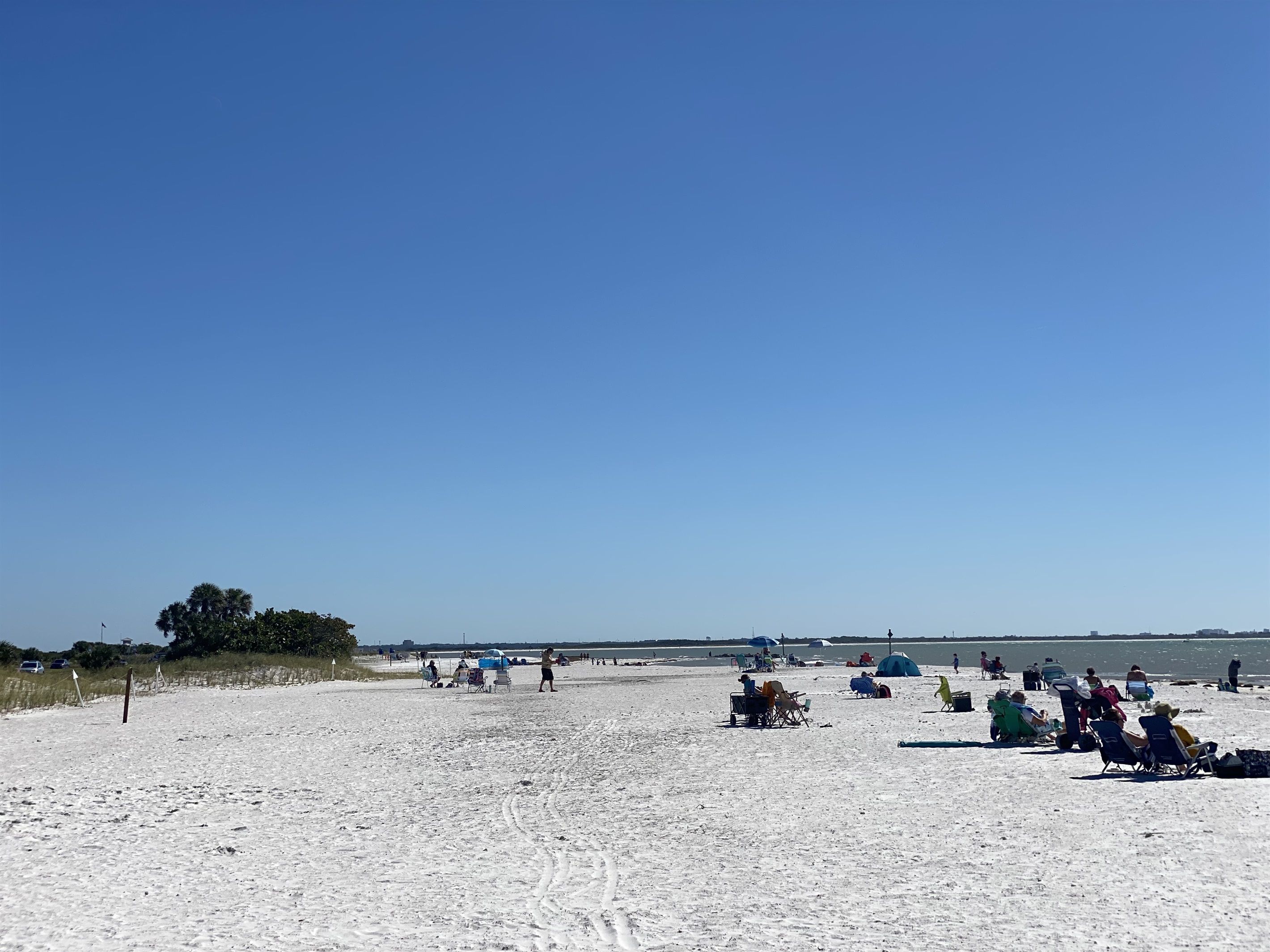 Una playa arenosa con gente relajándose, algunos en sillas y otros caminando.