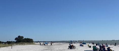 Una playa arenosa con gente relajándose, algunos en sillas y otros caminando.