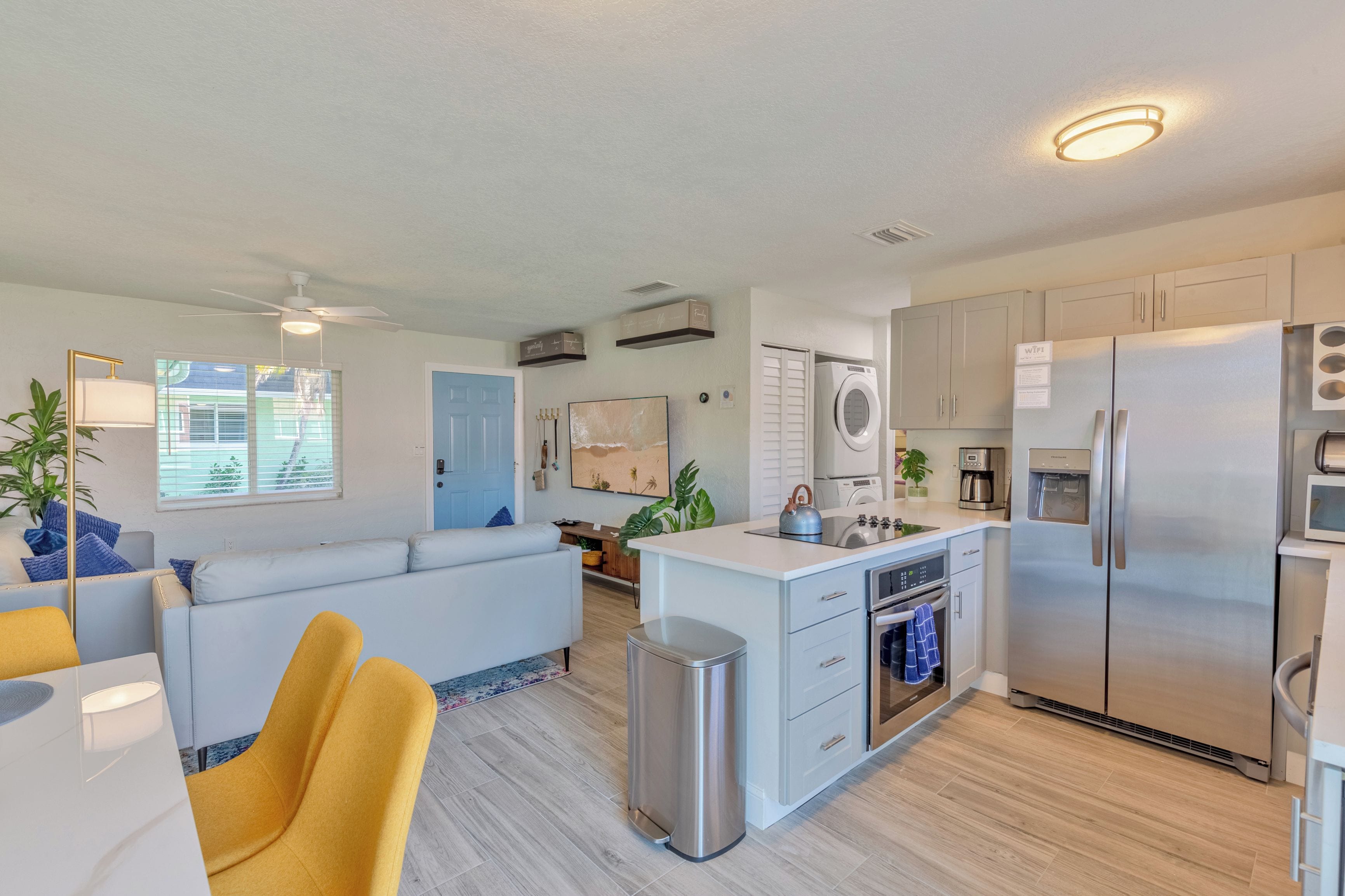 A modern kitchen with a central island, built-in appliances, and a dining area with yellow chairs.