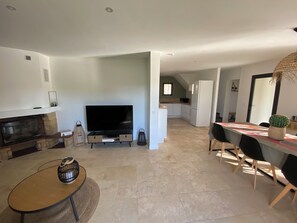 A modern living room with a flat-screen TV, a fireplace, and a dining area with a table and chairs.